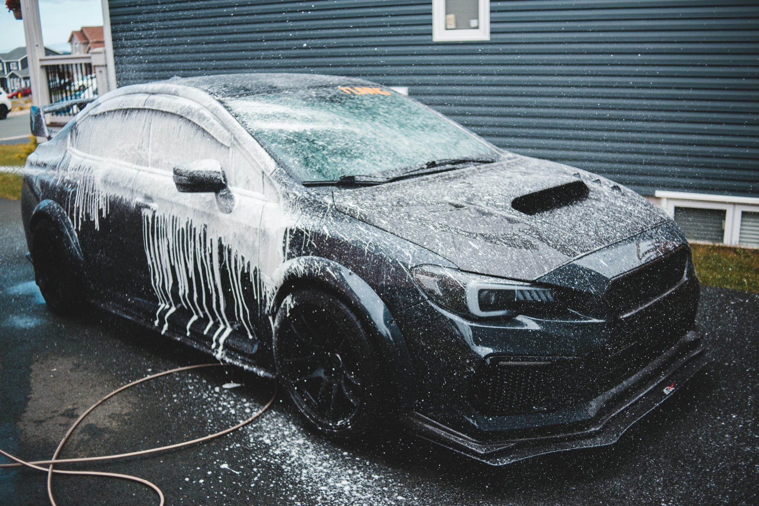 Black expensive tuned sports car under car wash next to cottage in daytime